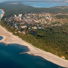 Jarosławiec atrakcje: malownicza plaża z falochronami, lasy sosnowe i zabudowania kurortu nad Bałtykiem.