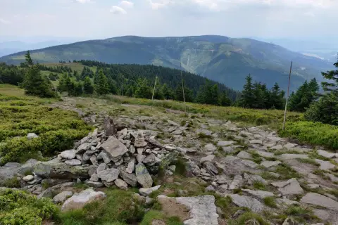 Kamienny szlak i kopczyk na górskim szczycie. W oddali widać zalesione pasma górskie, idealne miejsce na odkrywanie międzylesie atrakcje.