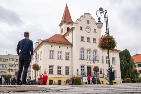 Mężczyzna podziwia ratusz w Trzebnicy, jedno z głównych atrakcji miasta. W tle zabytkowy budynek z zegarem i czerwonym dachem.