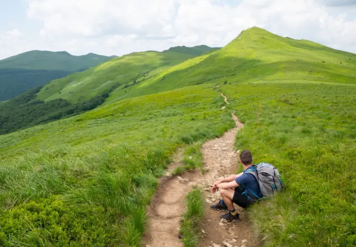 Turysta odpoczywa na szlaku, podziwiając zielone połoniny. Bieszczady atrakcje czekają!
