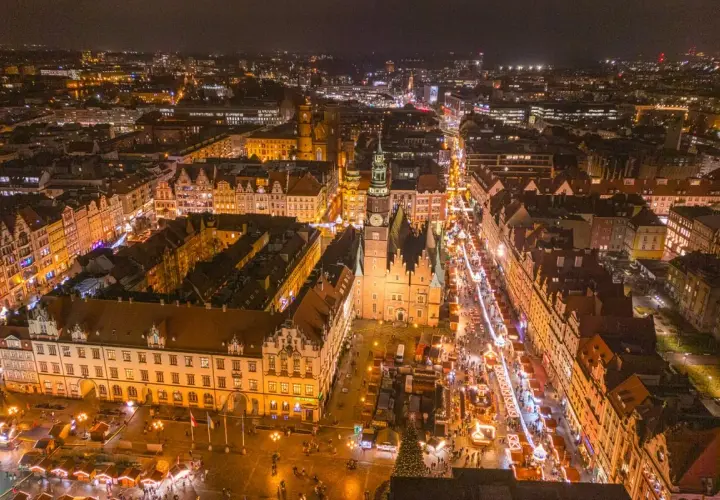 Nocny widok na Wrocławski Rynek, gdzie tętni życiem największy jarmark bożonarodzeniowy w Polsce. Kolorowe iluminacje i tłumy ludzi tworzą magiczną atmosferę.