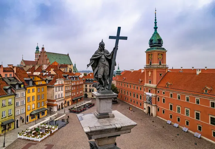 Pomnik króla Zygmunta III Wazy na placu Zamkowym, w tle Zamek Królewski i kolorowe kamienice Starego Miasta. Dwie wieże Warszawy w oddali.