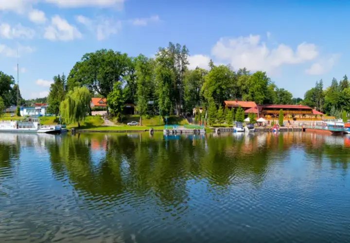 Malowniczy widok na port i jezioro w Rucianem Nidzie. Widać tu liczne łodzie, restauracje i zielone drzewa, tworzące idealne miejsce na wypoczynek i odkrywanie atrakcji.