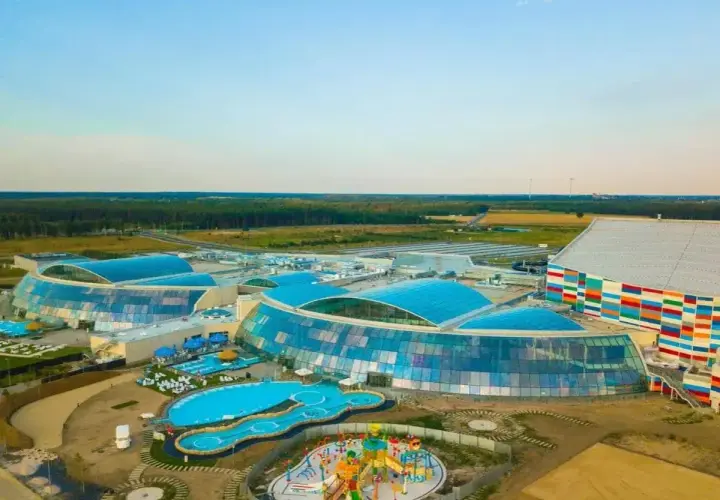 Nowoczesny park wodny Suntago z przeszklonymi dachami i kolorową fasadą, otoczony zielenią.