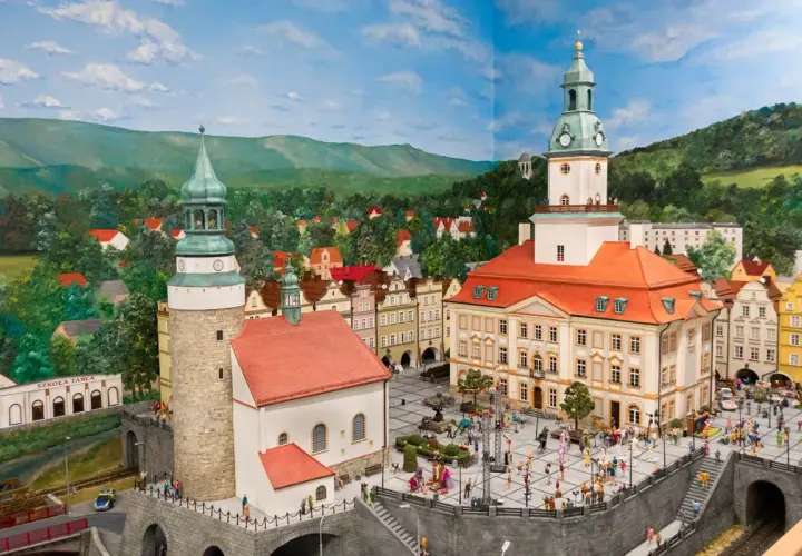 Miniaturowa panorama miasta z wieżami i placem pełnym ludzi. W tle góry i lasy, idealne na odkrywanie atrakcji w okolicy Jeleniej Góry.