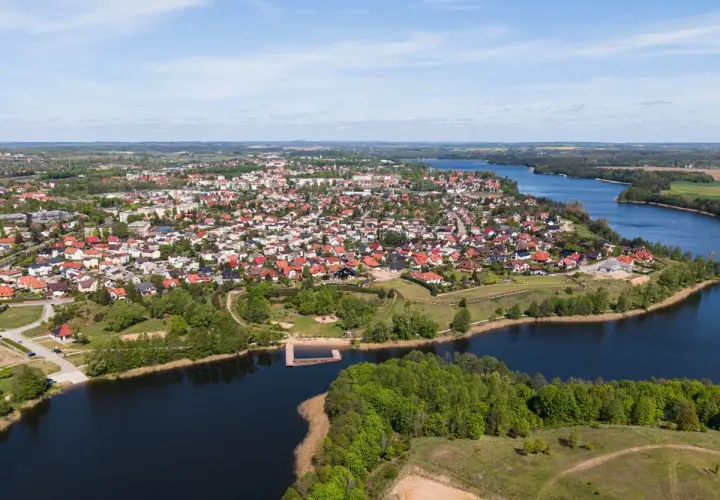 Widok z lotu ptaka na miasteczko nad jeziorem, jedno z największych rynków w Polsce, z domami z czerwonymi dachami i zielenią.