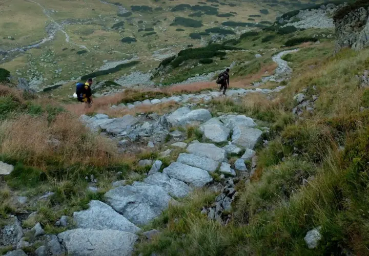 Dwóch turystów wędruje kamienistym szlakiem po zboczu górskim. Tatry atrakcje to wspaniałe widoki i wyzwania dla każdego miłośnika gór.