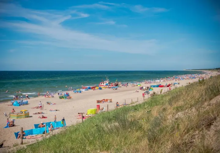 Słoneczna plaża w Dąbkach pełna turystów, kolorowych parawanów i łodzi. Idealne miejsce na wakacyjne atrakcje nad Bałtykiem.