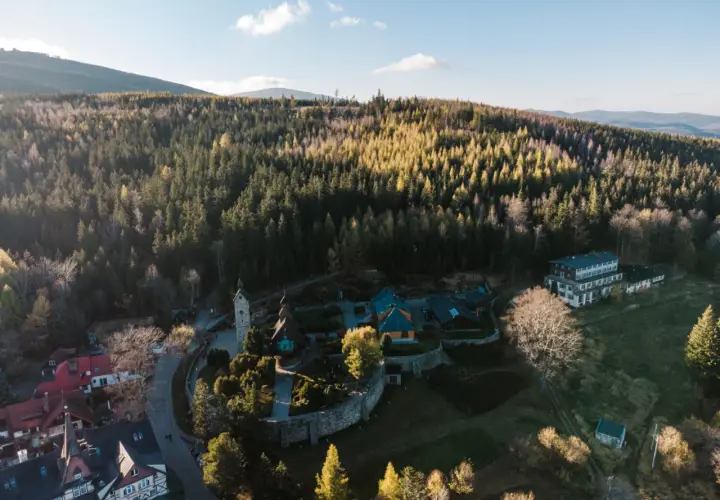Kolorowy kompleks budynków, w tym hotel i kościółek, otoczony lasem. To idealne miejsce na **centrum rekreacji i sportu**, gdzie można odpocząć wśród natury.