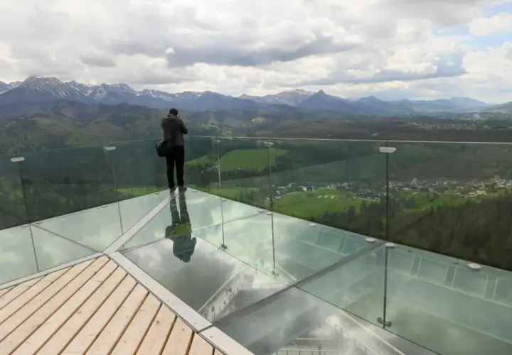 Mężczyzna na szklanej platformie wieży widokowej podziwia panoramę gór.