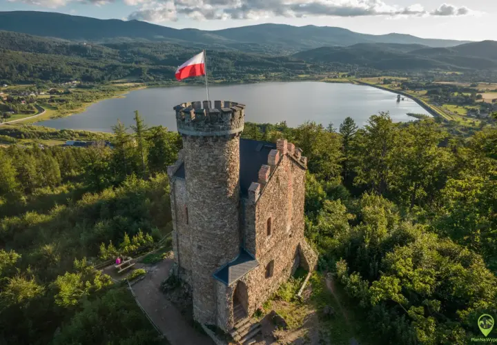 Kamienna wieża z polską flagą na szczycie, w tle jezioro i góry. Idealne miejsce, by odkryć, co warto zobaczyć w Sudetach.