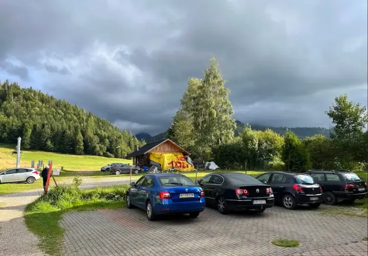 Samochody na parkingu pod Babią Górą, w tle las i chmury.