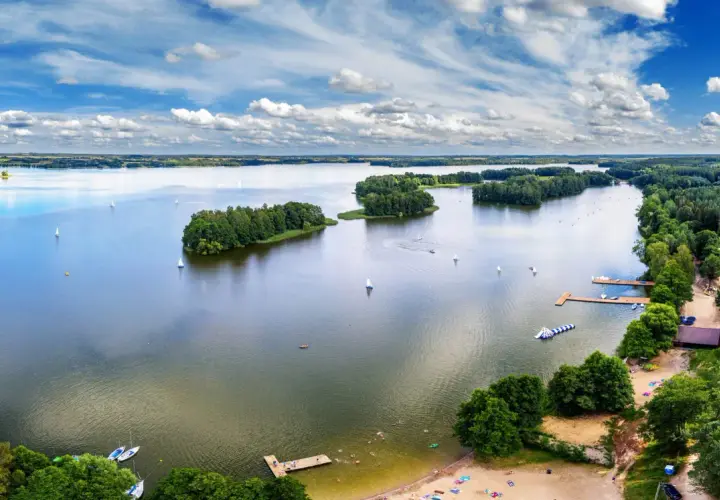 Idealne wakacje nad wodą: żaglówki, wyspy porośnięte drzewami i plażowicze cieszący się słońcem.