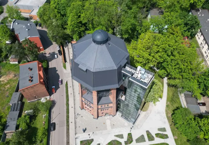 Nowoczesna wieża ciśnień w Zabrzu z przeszkloną windą i tarasem widokowym, otoczona zielenią.