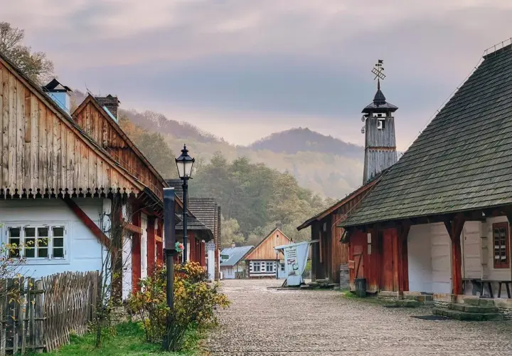 Sanok atrakcje: skansen z drewnianymi domami i wieżą, otoczony mglistymi wzgórzami.