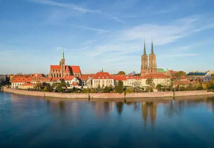 Widok na Ostrów Tumski, serce starego miasta Wrocławia, z katedrą i kościołem św. Krzyża odbijającymi się w spokojnej wodzie Odry.