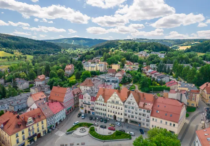 Urokliwy rynek i kolorowe kamienice w Dusznikach Zdroju. W tle zielone wzgórza, idealne na piesze wycieczki i odkrywanie atrakcji.