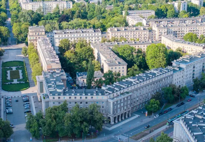 Osiedle bloków mieszkalnych w stylu socrealistycznym, z zielenią i ulicą, przypomina architekturę Nowej Huty.