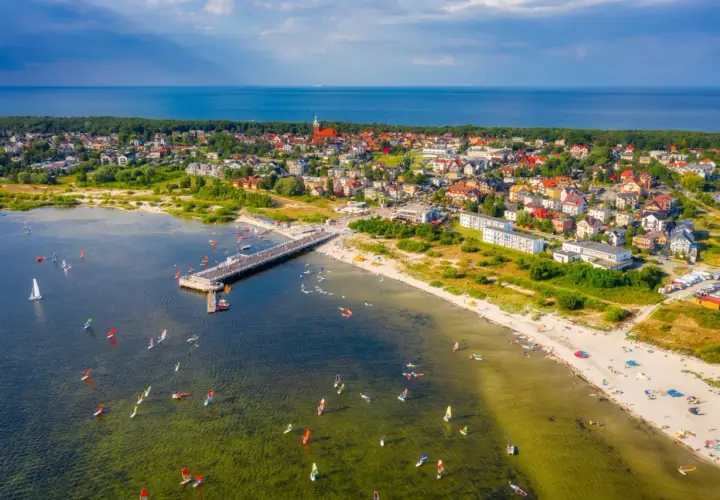 Jastarnia atrakcje: molo, plaża z turystami i liczne żaglówki oraz deski windsurfingowe na wodzie.