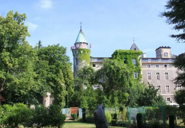 Zamek porośnięty bluszczem, z wieżą i zielonymi drzewami. Szczytna atrakcje turystyczne, które warto odkryć.