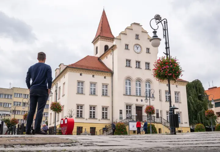 Mężczyzna podziwia ratusz w Trzebnicy, jedno z głównych atrakcji miasta. W tle zabytkowy budynek z zegarem i czerwonym dachem.