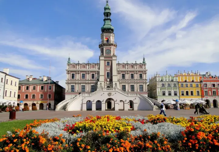 Zamość atrakcje: Ratusz i kolorowe kamienice na Rynku Wielkim, otoczone kwitnącymi rabatami.