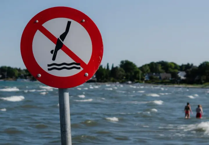 Znak zakazu kąpieli nad morzem. Dwie osoby w wodzie ignorują ostrzeżenie.