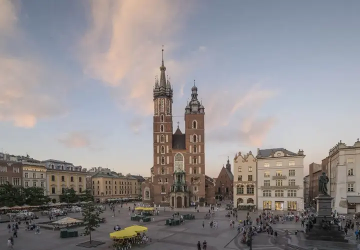 Majestatyczny kościół Mariacki na Rynku Głównym w Krakowie, otoczony kamienicami i placem tętniącym życiem.