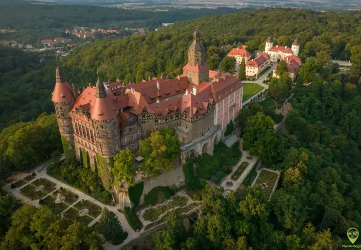 Zamek Książ otoczony lasami, z malowniczymi ogrodami i pobliską wsią. Rudawy Janowickie w tle.