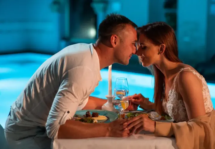 Romantyczna kolacja przy basenie, idealne fajne miejsca na sylwestra we dwoje. Para trzyma się za ręce, patrząc sobie w oczy.