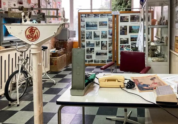 Wnętrze gabinetu lekarskiego z lat 70. XX wieku, część ekspozycji muzeum Dolny Śląsk. Widoczna waga lekarska, rower, aparat telefoniczny i zdjęcia.