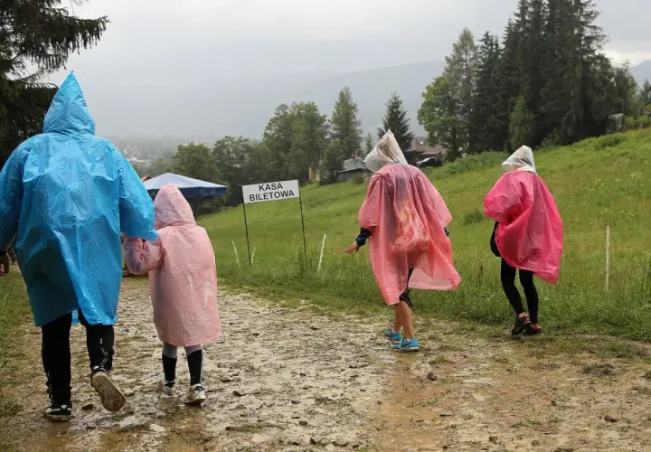 Rodzina w kolorowych pelerynach idzie błotnistą ścieżką. Nawet gdy pada deszcz, w Zakopanem można znaleźć ciekawe atrakcje.