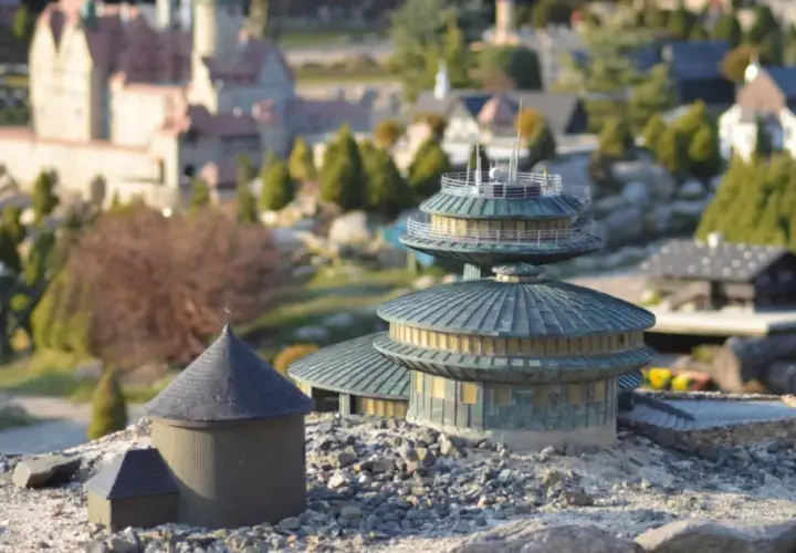 Miniaturowe budowle, w tym okrągły budynek z kopułą i wielopoziomowa konstrukcja, tworzą krajobraz jednego z parków miniatur w Polsce.