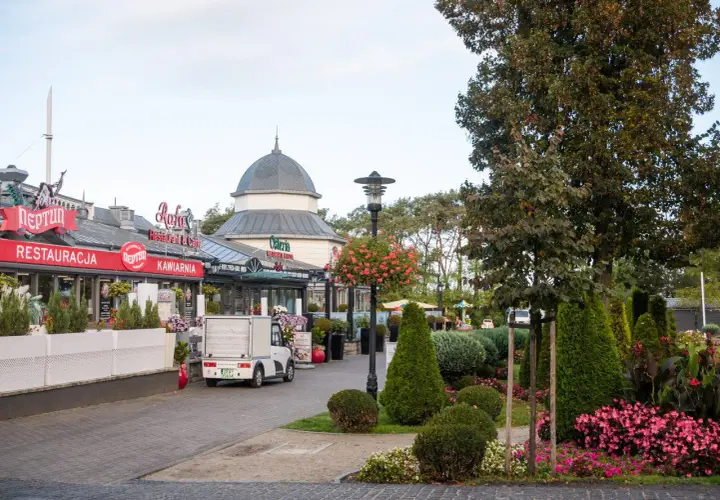 Ulica w Międzyzdrojach z restauracjami i kawiarniami, zielenią i ozdobnymi krzewami. Idealne miejsce na spacer i odkrywanie międzyzdrojskich atrakcji.