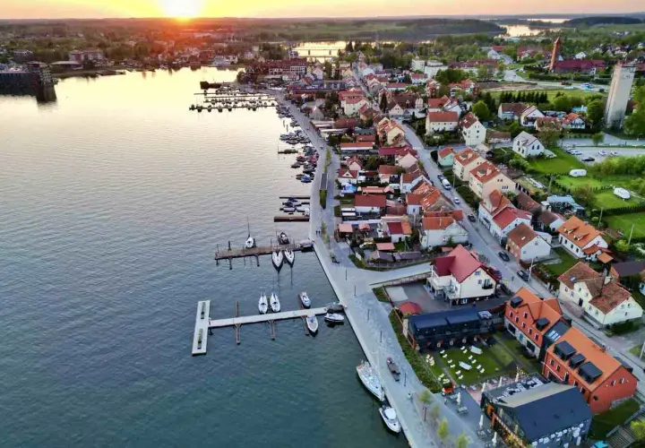 Zachód słońca nad jeziorem w Mikołajkach. Widok na port z łodziami i urokliwe miasteczko z czerwonymi dachami. Idealne miejsce na wakacyjne mikołajki atrakcje.