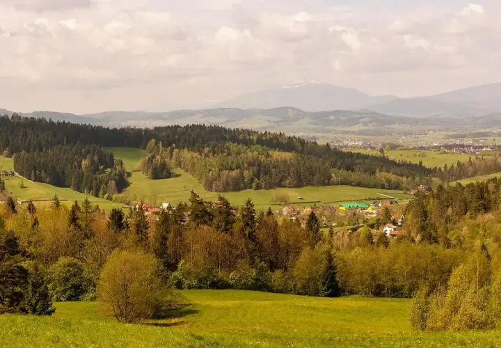 Malowniczy krajobraz z lasami i polami, w oddali widać góry i zabudowania. To idealne miejsce na odkrywanie rabka-zdrój atrakcje.
