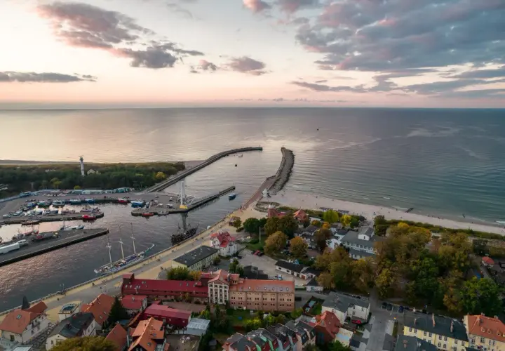 Widok na port i plażę w Ustce. Widać łodzie, latarnię morską i zabudowania. To jedne z wielu ustka atrakcje.