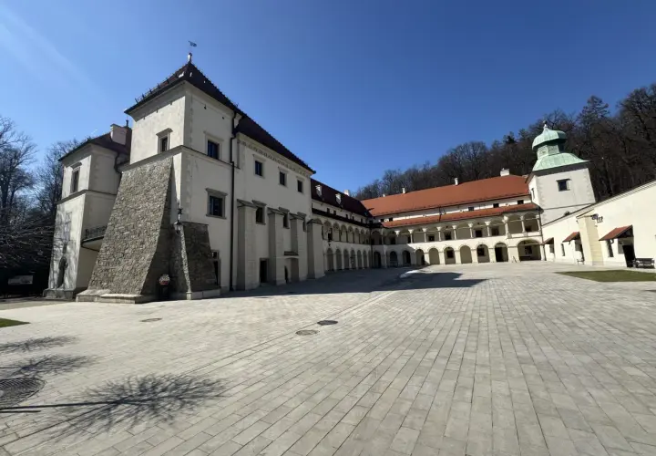 Zamek w Suchej Beskidzkiej, z dziedzińcem wyłożonym kamienną kostką i arkadowymi krużgankami, prezentuje się majestatycznie pod błękitnym niebem.