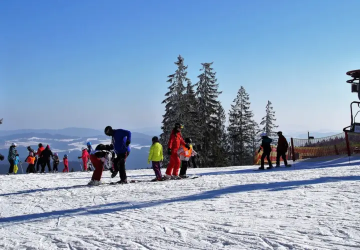 Słoneczny stok narciarski w Bieszczadach, z grupą narciarzy i snowboardzistów, w tym dzieci, przygotowujących się do zjazdu.