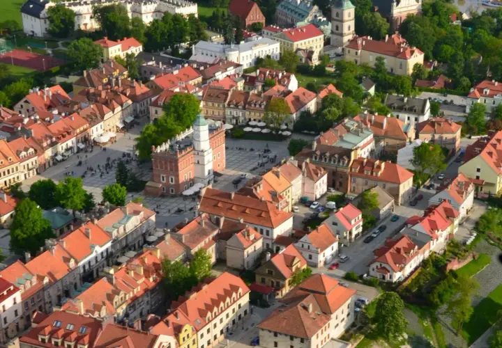 Urokliwe zabytkowe miasto nad Wisłą, z Rynkiem i wieżą ratuszową, otoczone kamienicami z czerwonymi dachami.