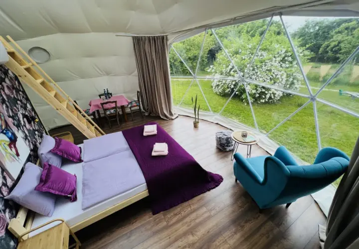 Przytulne wnętrze namiotu sferycznego z wygodnym łóżkiem i widokiem na zieleń. Idealne miejsce na glamping w Nałęczowie.