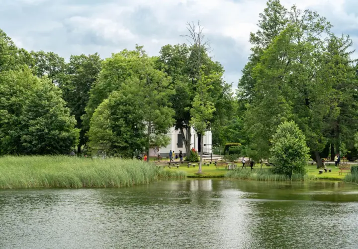 Malownicze jezioro i zielone tereny wokół białego budynku, idealne na spacer. Augustów atrakcje zachęcają do odpoczynku na łonie natury.