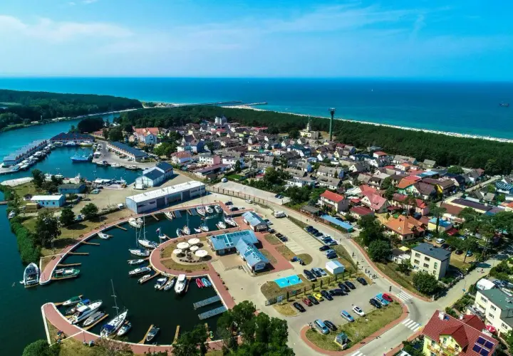 Widok z lotu ptaka na Dziwnów: port jachtowy, domy, las i morze. Wiele łodzi zacumowanych w marinie, idealne miejsce na wakacje.