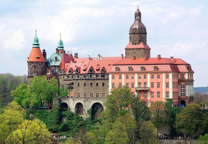 Imponujące zamki w okolicy Wrocławia, z wieżami i czerwonymi dachami, otoczone zielenią.