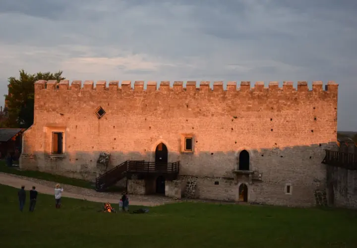 Zamek w Szydłowie o zachodzie słońca. Ludzie odpoczywają na trawie, podziwiając historyczne atrakcje.