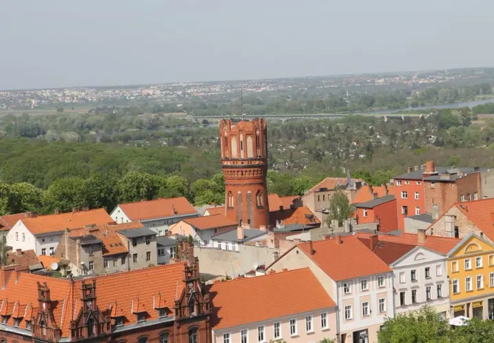 Widok na Chełmno z charakterystyczną wieżą ciśnień. Miasto z czerwonymi dachami i zielenią w tle. Chełmno atrakcje warte zobaczenia.
