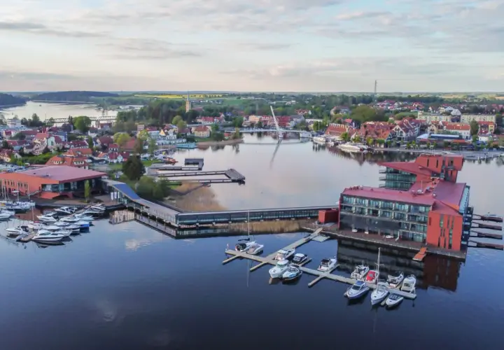 Malownicze mazury miejscowości z nowoczesną architekturą nad jeziorem, pełne łodzi i jachtów.