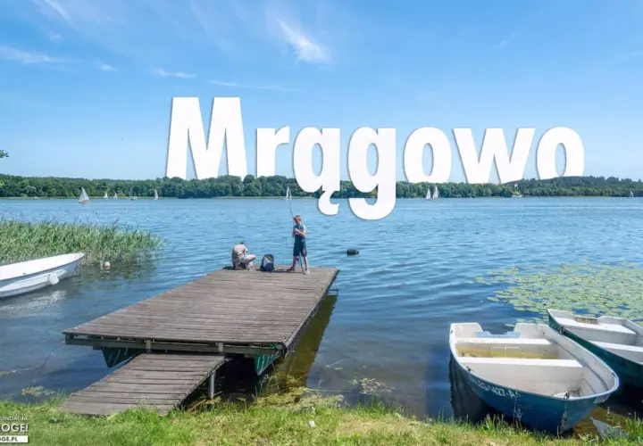 Mrągowo atrakcje: spokojny dzień nad jeziorem, dzieci łowią ryby z pomostu, żaglówki na horyzoncie.
