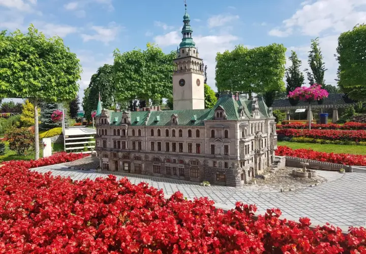 Miniatura ratusza z wieżą i zegarem, otoczona czerwonymi kwiatami. Jedna z wielu kłodzko atrakcje.
