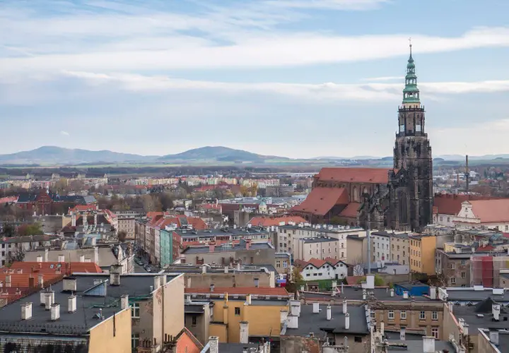 Widok na miasto z dominującą wieżą kościoła. W oddali góry. **Świdnica atrakcje** zachwycają.